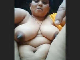 A mature woman bares her breasts and pussy in a village setting
